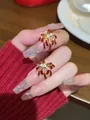 Macro shot of gold spark ring with red zircon tips and festive glitter nails on wood - Style 8 (Gold Pin - Red)
