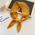 Pleated mustard yellow square scarf styled as a necktie knot on a minimalist stand - Orange