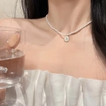 Elegant pearl necklace with oval floral metal pendant worn on a model's neck - Pearl Flower Necklace (X2866) / Cream