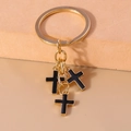 Detail of gold keychain with three black enamel cross pendants on geometric background - Black