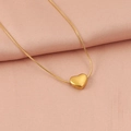 Primer plano del colgante de corazón dorado y cadena de serpiente sobre tela rosa - Dorado