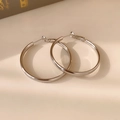 Dettaglio di orecchini a cerchio argento lucido con ombra naturale su sfondo beige - Argento