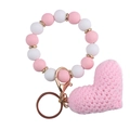 Detailed shot of a pink knitted heart charm and beaded wristband keychain with gold rings - Pink