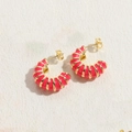 Golden C-shaped hoop earrings featuring vibrant hot pink enamel stripes and ribbed texture - Red