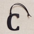 Close-up of black leather letter C bag charm with matching strap on beige linen - C Letter Black