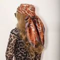 Detail of brown paisley satin scarf tied on head, showing the soft fabric texture - Orange