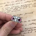 Macro shot of vintage silver owl ring featuring striking pink eyes on a retro paper backdrop - Pink