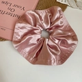 Detail eines rosa Satin-Haargummis mit weichen Stofffalten und Perlenkette im Hintergrund - Rosa