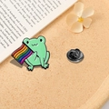 Detail view of cartoon green frog enamel pin with rainbow flag on a beige background - Alloy / Frog Holding Flag