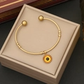Dettaglio del bracciale rigido dorato con ciondolo occhio greco in scatola beige - Arancione