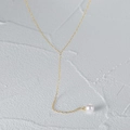 Detail of gold-plated Y-shaped necklace with a white pearl pendant on a grey rock surface - Gold Y-Shape-Thin Chain Pearl Structure