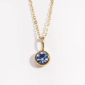 Primer plano de un collar dorado con un brillante colgante redondo de piedra natal azul - Marzo Azul Claro