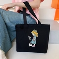 Black canvas tote bag with girl and cat illustration, shown on model in minimal studio - Straw Hat Girl - Black