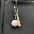 Mini baseball keychain with white leather ball and wooden bat hanging on black bag - White