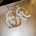 Close-up of interlocking gold metal rings and white pearl hoops with crystal earring hooks - Gold