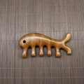 Macro shot of polished sandalwood meridian massage comb with a smooth finish and wood grain - Golden Sandalwood Whale with Hole (11*5.5*1.8cm)