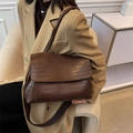 Brown crocodile pattern shoulder bag with flap design and fabric strap worn by a model - Coffee