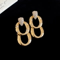 Détail de boucles d'oreilles ovales dorées avec texture martelée et zircons étincelants - Or