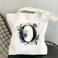 White canvas tote bag with floral letter O print on a black metal chair against grey wall - Letter O / 35*40cm