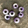 Amethyst natural stone beads in purple and white texture on dark rock surface - Amethyst