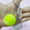 Close-up of yellow tennis ball and silver metal racket keychain held against pink background - 3.8cm Ball / Green