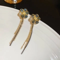 Dettaglio di orecchini a fiore con nappe, gemme grigio-blu e catene d'oro su piatto bianco - Fiore Oro-Blu (Perno in Argento)