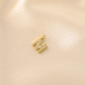 Macro shot of gold letter M pendant with clear zircons on champagne silk background - Letter M / Gold
