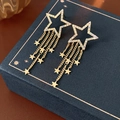 Detailed view of gold star tassel earrings with shimmering crystals on a blue jewelry box - Gold (Real Gold Plated Silver Pin)