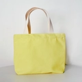 Detail of yellow canvas tote bag with beige handles on minimalist white background - Open Top / Yellow