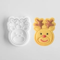 White plastic reindeer head cookie mold and decorated gingerbread biscuit on white surface - Deer C