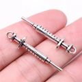 Silver syringe charm pendant with detailed scale marks held on a fingertip for scale - Antique Silver