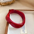 Macro detail of a chunky red acrylic wave bangle with smooth translucent resin texture - Red - Twisted