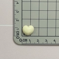 Close-up of a 1.2cm x 1cm glossy macaron beige resin heart charm on a scale - Off White