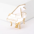 Detailed close-up of a white enamel piano brooch with elegant golden metallic accents - White