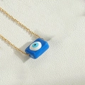 Golden necklace with a rectangular blue evil eye pendant on a textured white background - Sapphire Blue