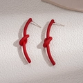 Détail des boucles d'oreilles nœud rouge mat avec tiges en argent sur fond texturé - Rouge
