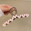 Brown translucent hair claw clip with pink heart motifs held by hand in warm studio light - 13cm / Pink