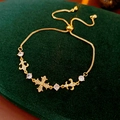 Dettaglio del bracciale dorato con croce e giglio decorato con zirconi bianchi lucidi - Stile Croce a Strato Singolo / Oro