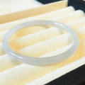 Elegant round grey-white jade bangle bracelet displayed on a soft beige velvet jewelry box - Extra Thin: Light Grey 60mm Diameter Bangle