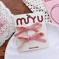 Detailed view of pink satin bow hair clips on a white card in a cozy setting - Korean Pink