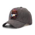 Vue détaillée de l'ours en peluche brun et du charme cerise sur la casquette usée - Taille unique / Gris
