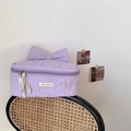Gesteppte hellviolette Kosmetiktasche mit Blumenmuster und großer Schleife auf einem Stuhl - Gesteppte Blume Lila