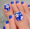 Dettaglio di unghie finte per piedi blu navy con design floreale bianco sulla spiaggia - FW97