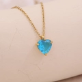 Goldene Herzkette mit einem facettierten blauen Edelsteinanhänger auf beigem Grund - März / Seeblau (5722226372625)