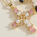 Macro detail of cross pendant featuring pink gems and white pearl on 14K gold plated base - Pink