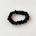 Detail van zwarte satijnen scrunchie met glanzende zijden textuur op wit leer oppervlak - Zwart