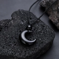 Minimalist black crescent moon pendant with black hand-woven rope on volcanic rock background - Black