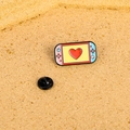 Süße Emaille-Anstecknadel in Rosa und Blau als Spielkonsole auf Kork-Hintergrund - Handheld-Konsole
