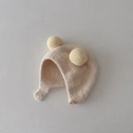 Detail of soft knit baby earflap hat with dual yellow pom-poms and wood button closure - Beige
