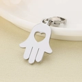 Detailed macro view of silver Hamsa Hand pendant with lobster clasp on beige base - 22X15mm Heart Hollow Hamsa Hand Style(KLJ7006-Z) / Silver